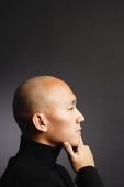 Man with shaved head, hand on chin, looking away - Asia Images Group