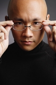Man with shaved head, adjusting glasses, looking at camera - Asia Images Group