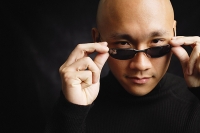 Man with shaved head, adjusting sunglasses, looking at camera - Asia Images Group