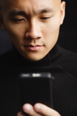 Man with shaved head, looking at mobile phone, selective focus - Asia Images Group