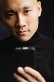 Man with shaved head, holding mobile phone, looking at camera selective focus - Asia Images Group