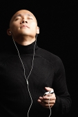 Man with shaved head, listening to music with earphones, eyes closed - Asia Images Group