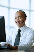 Man with headset, smiling, using computer - Asia Images Group