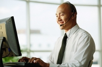 Man with headset, using desktop PC, smiling - Asia Images Group