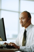 Man with headset, in front of computer, smiling - Asia Images Group