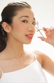 Woman holding eyelash curler to eye, looking at camera - Asia Images Group