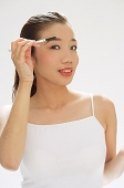Woman holding brush to eyebrows, looking at camera - Asia Images Group