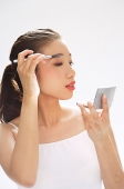 Woman holding brush to eyebrows, looking at compact mirror - Asia Images Group