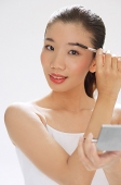 Woman holding brush to eyebrows, compact mirror on other hand - Asia Images Group