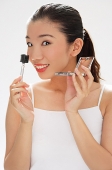 Woman holding eyebrow brush and compact, smiling at camera - Asia Images Group