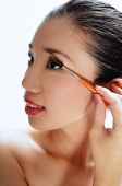 Woman applying mascara, looking away - Asia Images Group