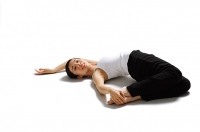 Woman lying on back, pulling feet towards her, looking at camera - Asia Images Group