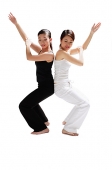 Two women back to back, bending knees, arms outstretched - Asia Images Group