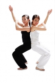 Two women back to back, bending knees, arms outstretched, smiling at camera - Asia Images Group