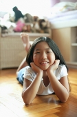 Girl in bedroom, lying on floor, hands on chin, looking at camera - Asia Images Group