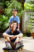 Father sitting on floor, son behind him, looking at camera - Asia Images Group