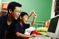 Father and son looking at computer, raising hands - Asia Images Group