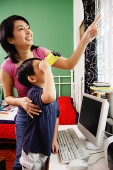 Mother and son standing side by side, son using binoculars, mother pointing at window - Asia Images Group