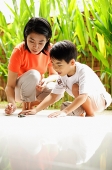 Mother and son crouching, looking at terrapin on floor - Asia Images Group