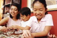 Mother with two children, fixing jigsaw puzzle pieces - Asia Images Group