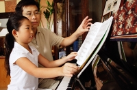 Father and daughter sitting at piano, looking at music sheets - Asia Images Group