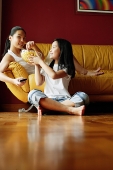 Two sisters sitting in living room, eating popcorn - Asia Images Group