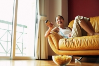 Girl lying on sofa, holding remote control - Asia Images Group
