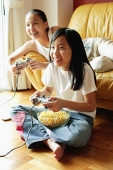 Two sisters in living room, playing video games - Asia Images Group