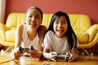 Two sisters in living room, lying on floor playing video games - Asia Images Group