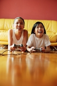 Two sisters lying on floor playing video games - Asia Images Group