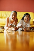 Two sisters lying on floor playing video games, smiling - Asia Images Group