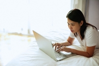 Woman lying on bed, using laptop - Asia Images Group