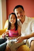 Father and daughter looking at camera, holding video game controllers - Asia Images Group