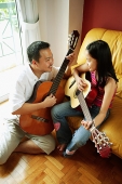 Father and daughter holding guitars, sitting face to face - Asia Images Group