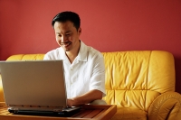 Man sitting on sofa, using laptop - Asia Images Group