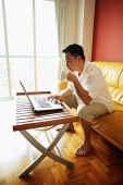 Man using laptop, drinking from mug - Asia Images Group