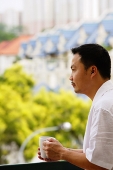 Man leaning on railing, looking away, holding mug - Asia Images Group