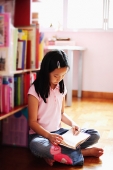 Girl sitting cross-legged in bedroom, reading book - Asia Images Group