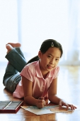Girl lying on floor, with paper and crayons, looking at camera - Asia Images Group