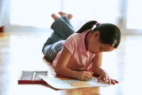 Girl lying on floor, drawing on paper with crayons - Asia Images Group