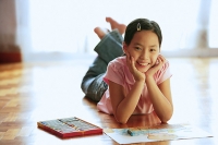 Girl lying on floor, with paper and crayons, looking at camera, portrait - Asia Images Group