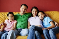 Family of four sitting on sofa, looking at camera - Asia Images Group