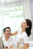 Couple in bedroom, breakfast tray on bed, woman smiling, looking up - Asia Images Group