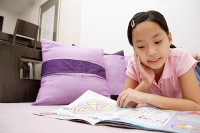 Girl reading magazine, lying on front, hand on chin - Asia Images Group