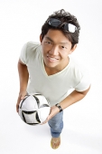 Young man in T-shirt and jeans, holding soccer ball, smiling at camera - Asia Images Group