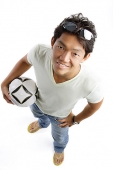 Young man in T-shirt and jeans, holding soccer ball, smiling at camera, hands on hip - Asia Images Group