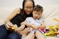 Mother and daughter on sofa, playing with toys - Asia Images Group