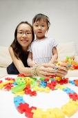 Mother and daughter looking at camera, toy pieces in front of them - Asia Images Group