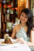 Woman at restaurant, sitting at table with food, looking at camera - Asia Images Group