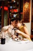 Couple in Chinese restaurant, toasting with wine glasses, man kissing woman on cheek - Asia Images Group
